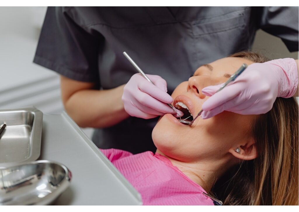 Dentist performing oral exam on patient in dental chair using mirror and dental tools.