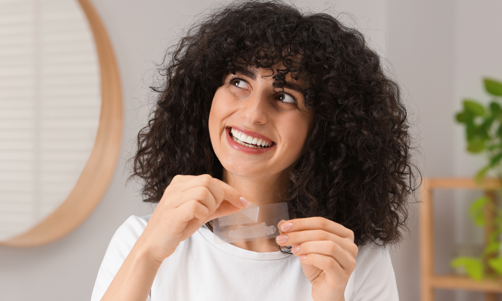 woman smiling while holding teeth whitening strips before application at home