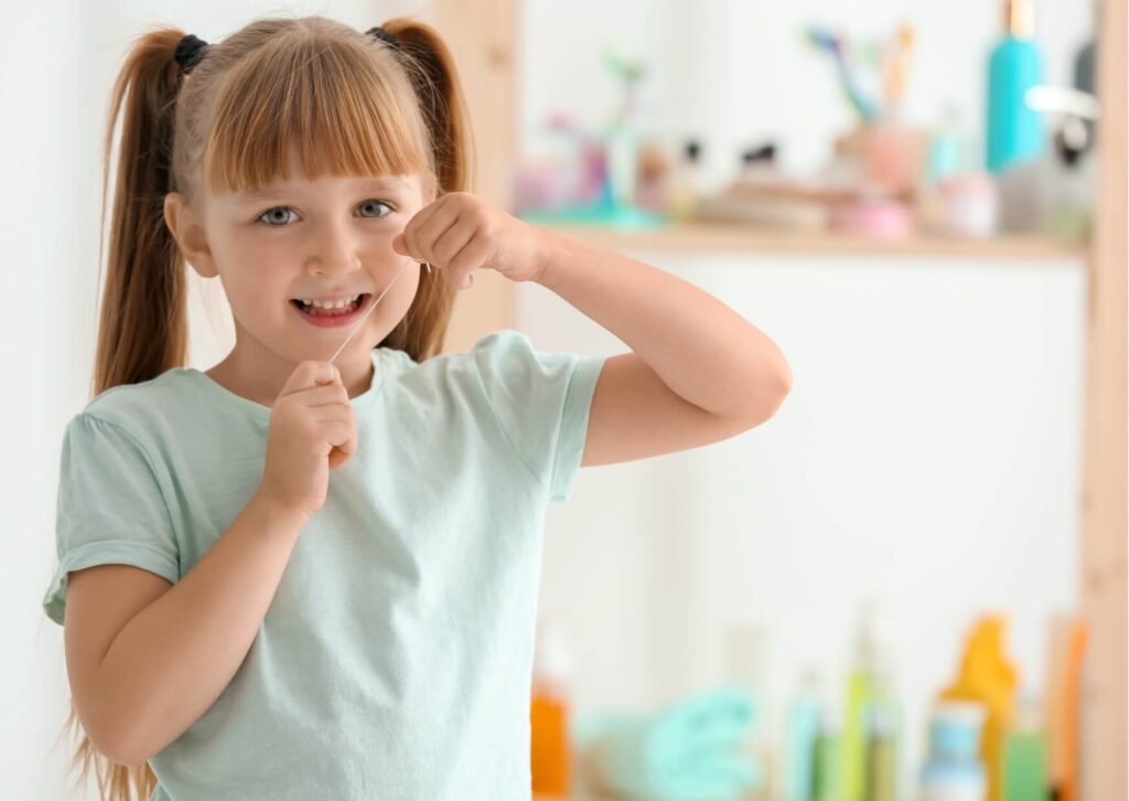 Young girl flossing her teeth at home, highlighting the importance of early dental care and knowing when to take your child to the dentist.