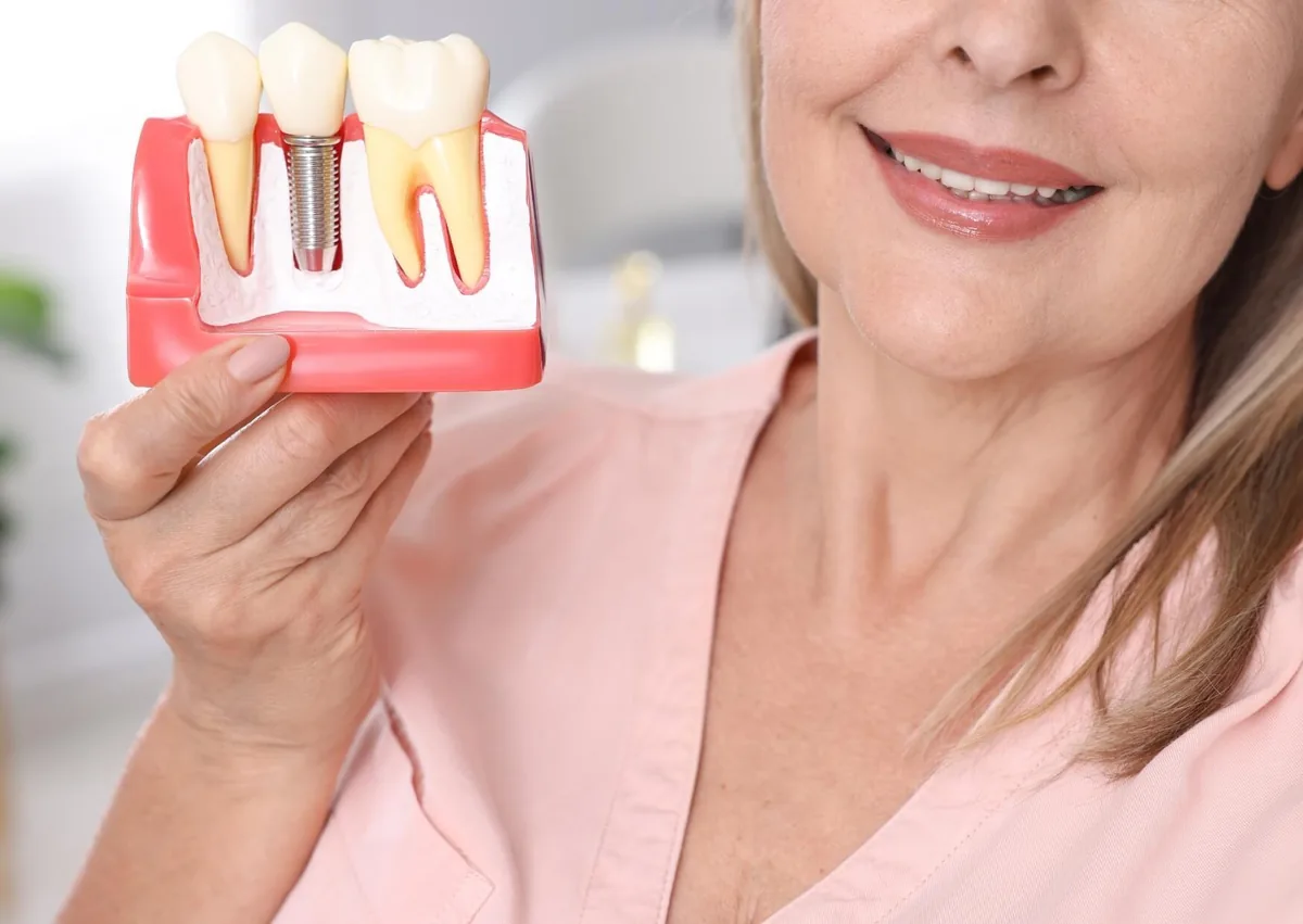 Woman holding a dental model showing how a dental implant replaces a missing tooth.
