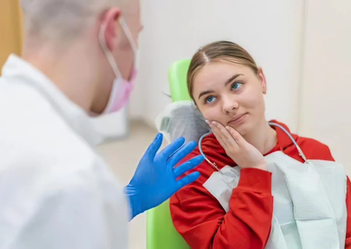 Patient experiencing mouth discomfort while discussing what to eat after wisdom teeth removal with a dentist.